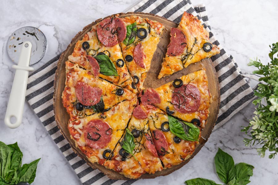 Looking down on a whole pepperoni pizza with a slice pulled out and a pizza cutter nearby.