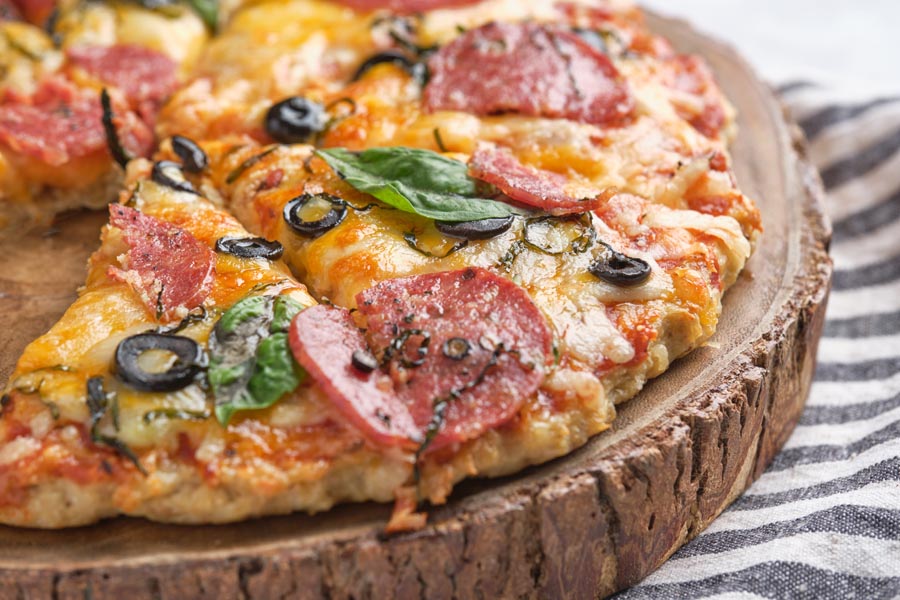 Closeup of a keto pizza topped with basil, olive and pepperoni.