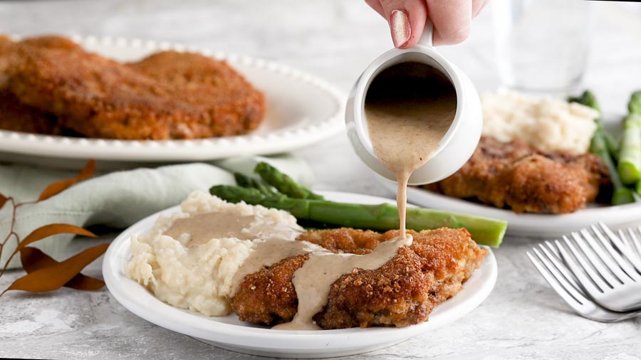 pouring gravy on a thick keto fried steak out of a white gravy boat