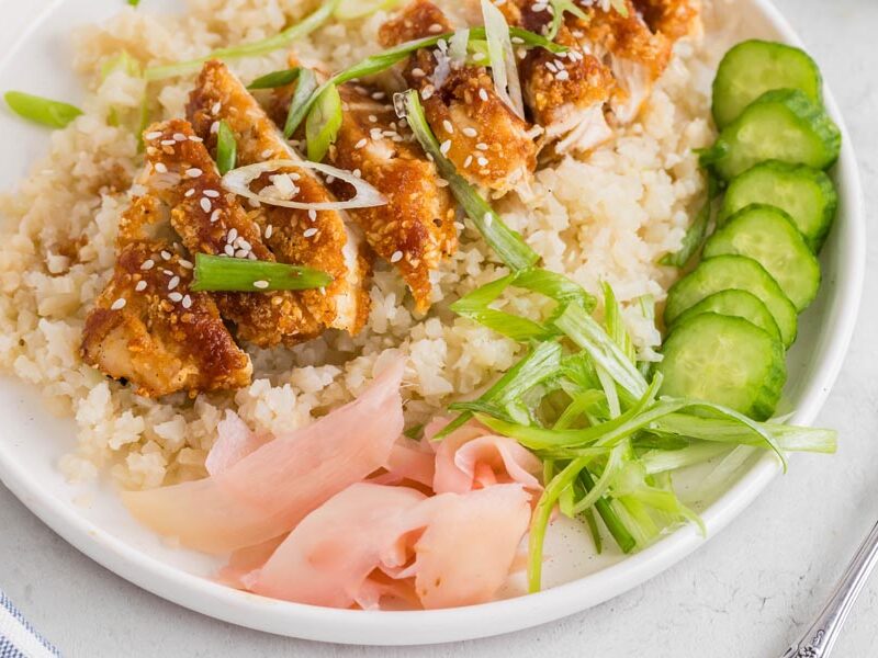 Close up of sesame and panko crusted chicken over cauliflower rice and topped with sliced onion.