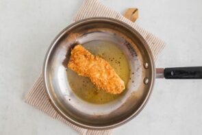 A breaded piece of cooked chicken in a skillet.