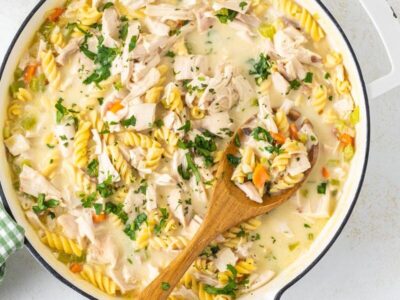A wooden spoon holding a serving of chicken noodle casserole in a skillet.