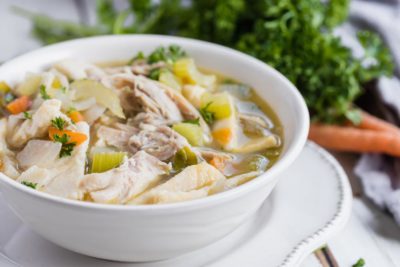 a large bowl of chicken noodle soup with parsley in the background