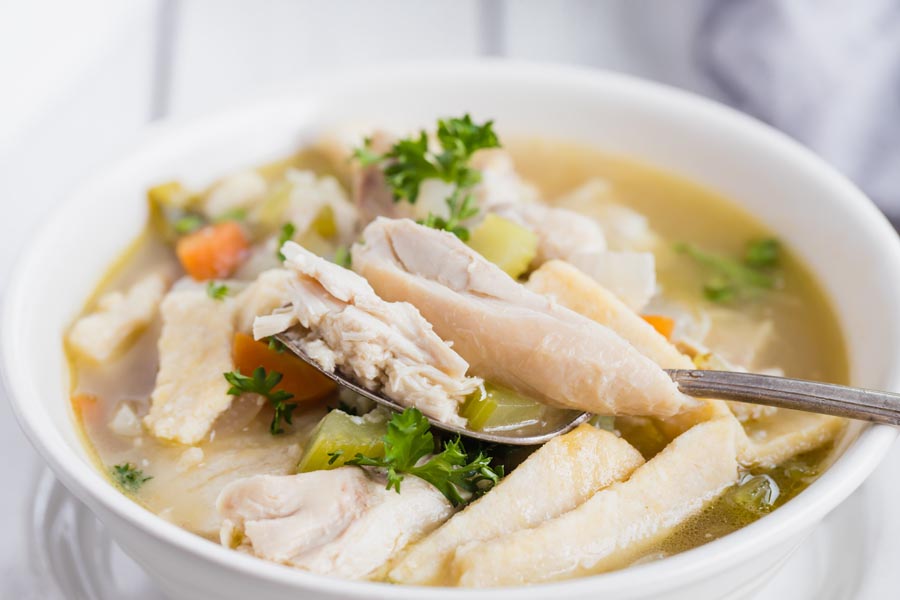 a spoonful of chicken and vegetables sitting over chicken soup