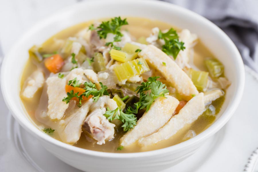 a bowl of chicken noodle soup topped with parsley