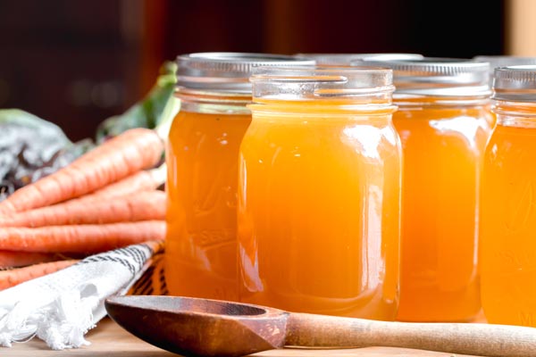 pint glasses with chicken bone broth in them and carrots nearby