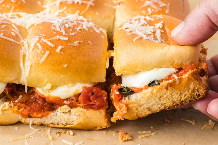 A close-up of keto chicken parmesan sliders with marinara sauce and melted mozzarella, as one slider is being pulled from the tray.