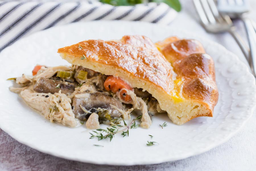 a close up of a slice of chicken pot pie on a plate with carrot and mushroom spilling out