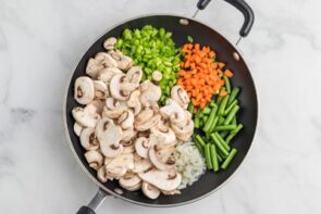 A skillet with sliced mushrooms, green beans, celery and chopped carrots.