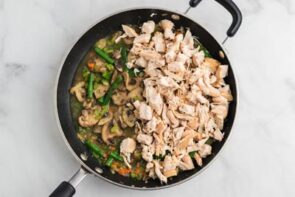 Cooked diced chicken sitting in a skillet with cooked veggies and broth.