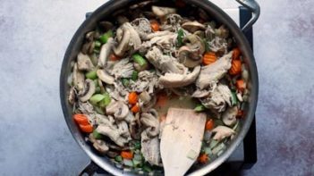 a wood spoon stirs a mixture of shredded chicken and vegetables in a skillet