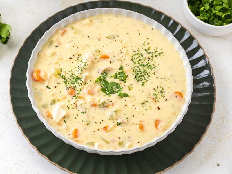 A bowl of low-carb of creamy chicken and rice soup topped with fresh herbs.