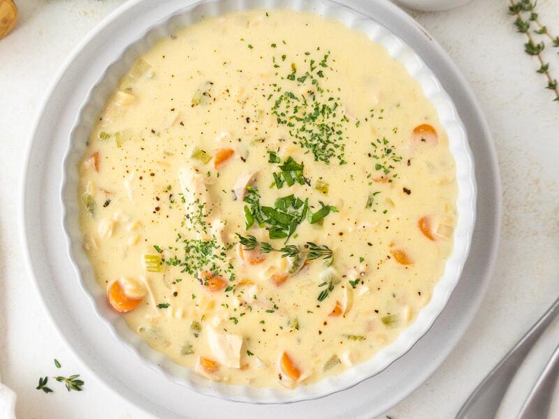 Looking down into a creamy soup filled with chicken, carrot and fresh herbs.