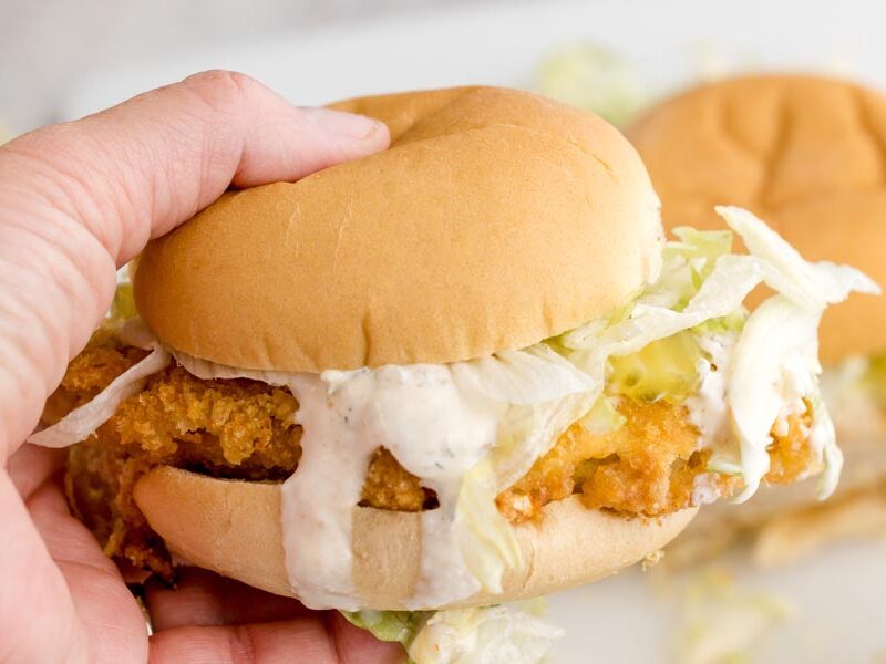 A hand holding a keto McChicken sandwich filled with a crispy chicken patty, lettuce, pickles, and creamy sauce.