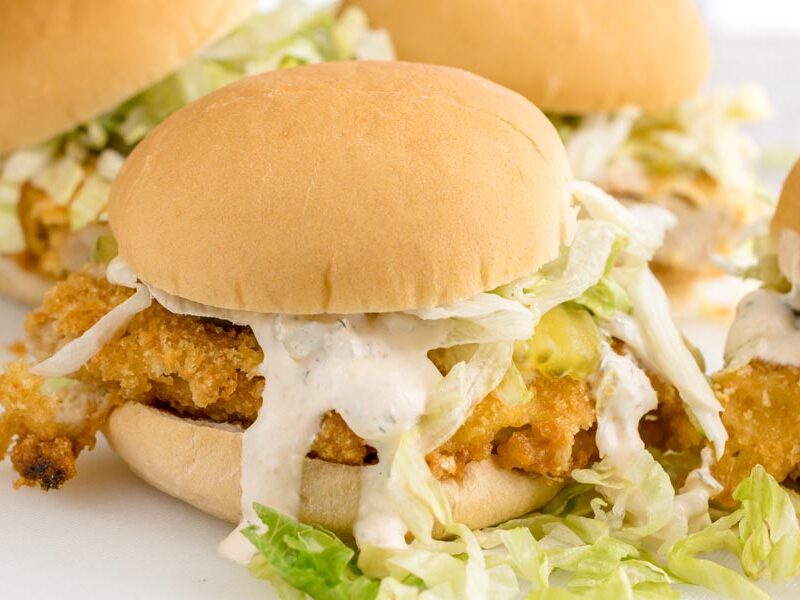 Close-up of a keto McChicken sandwich with a crunchy chicken patty, shredded lettuce, pickles, and creamy sauce dripping over the bun.
