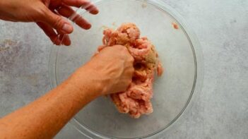 Ground chicken being mixed with seasonings in a glass bowl to make a giant keto McChicken patty.