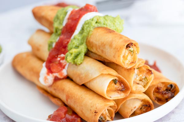 a plater of chicken taquitos topped with salsa and guac