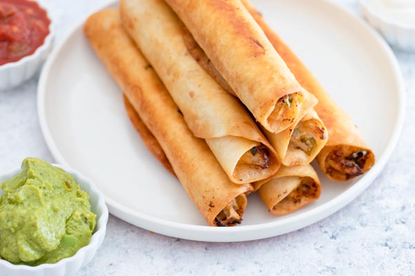 a plate of rolled crunchy keto taquitos next to salsa and sour cream