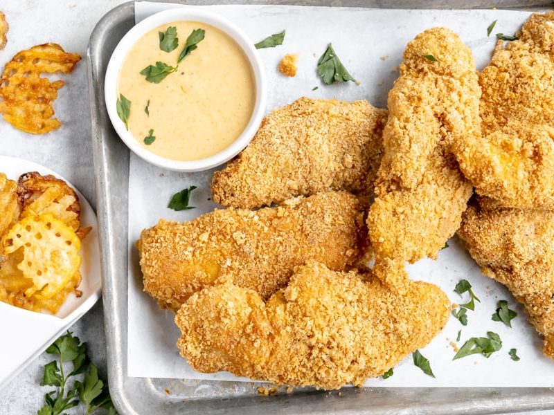 a tray with a bunch of baked chicken strips next to waffle fries and chick-fil-a sauce