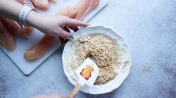 stirring a breading mixture in a small white bowl with a spatula with a honey bear on it