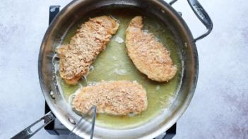 three breaded chicken strips frying in a skillet with oil