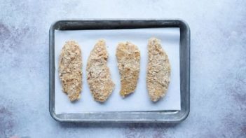 four breaded chicken tenders on a baking tray lined with parchment paper