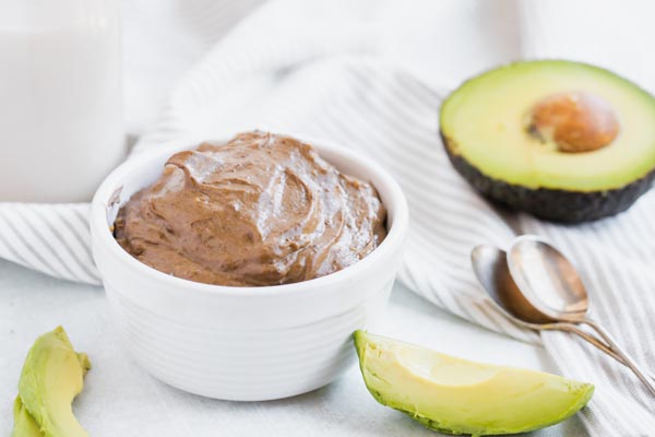 creamy chocolate keto pudding in a white bowl with avocado slices nearby