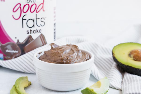 chocolate pudding in a white bowl with a container of love good fats protein in the background