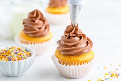 piping a swirl of keto chocolate frosting on a white cupcake