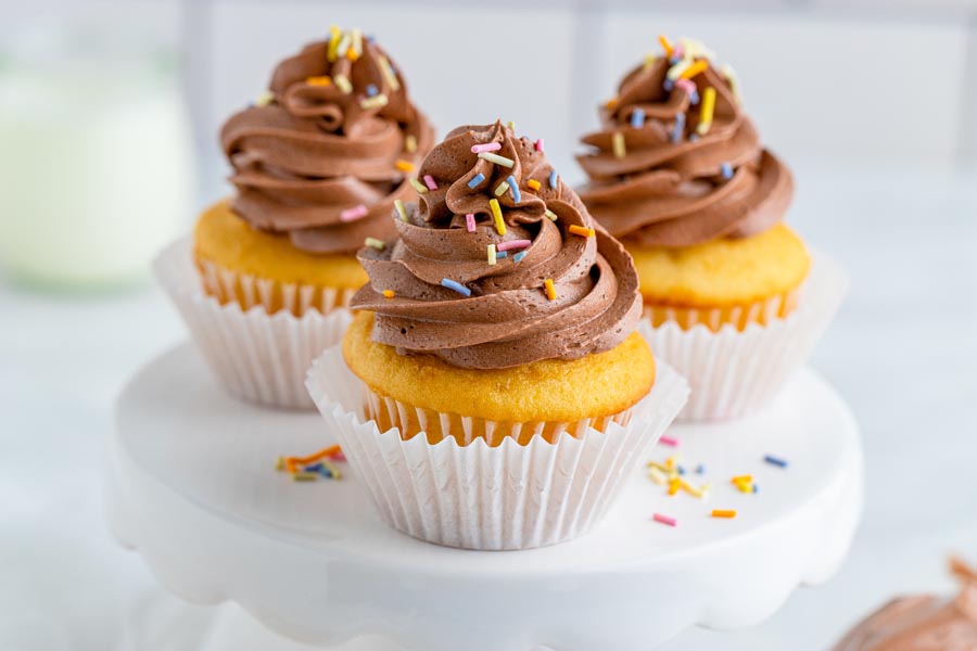 three vanilla cupcakes with keto butter cream frosting on a cake stand