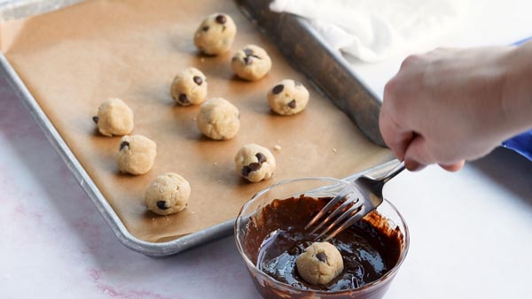 dipping the ball of cookie dough into melted chocolate to coat