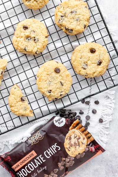 chocolate chip cookies cooling on a wire rack with a bag of chocolate chips below and chocolate chips spread around