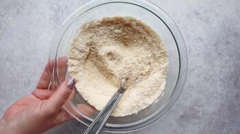 almond flour in a bowl with a whisk and a hand grabbing the bowl