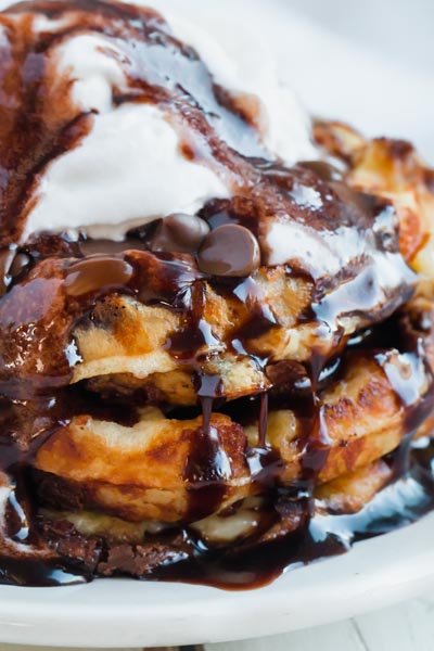 chocolate syrup dripping down three waffles topped with whipped cream