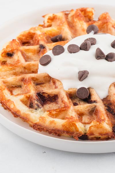 a crispy waffle topped with a dollop of whipped cream and chocolate chips