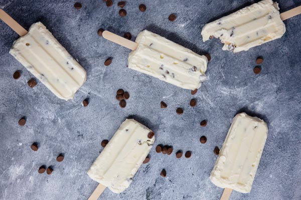 five frozen yogurt bars on a blue surface with chocolate chips scattered