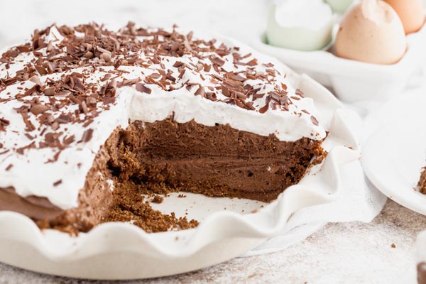 a couple slices of pie missing from a chocolate cream pie with eggs in the background