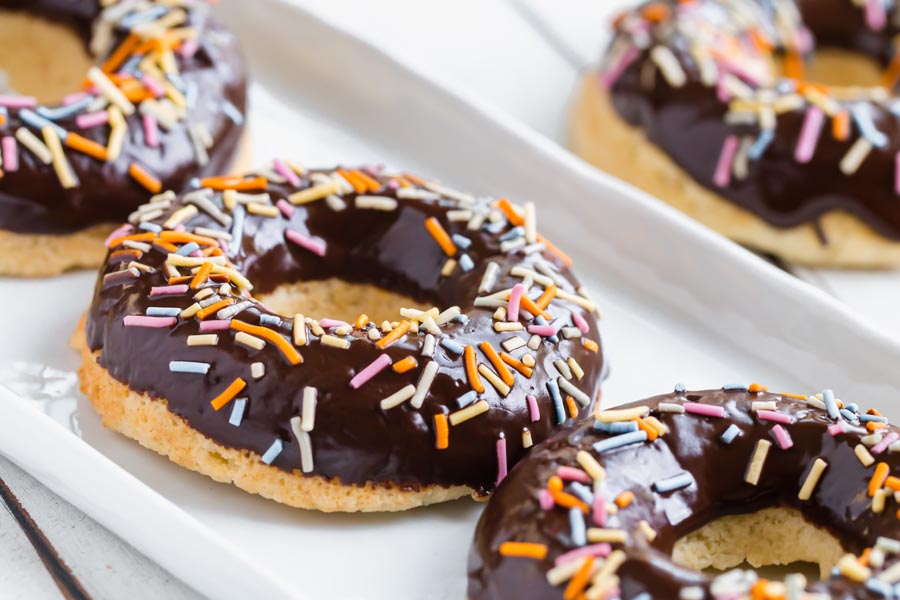 two shiny chocolate covered donuts with sugar free sprinkles on a white plate