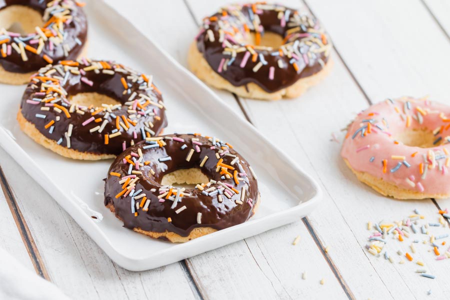 chocolate and pink glazed donuts on a white counter with sprinkles all over
