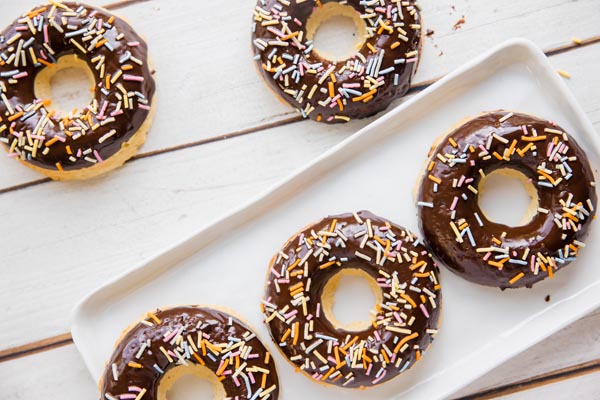 five chocolate glazed donuts with sprinkles on a white board and rectangle plate