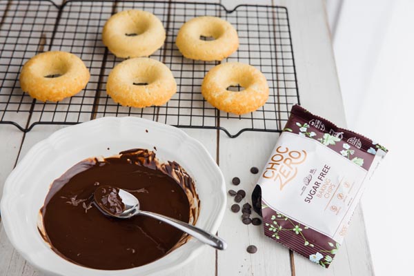 a bowl of melted dark chocolate with keto donuts on a wire rack