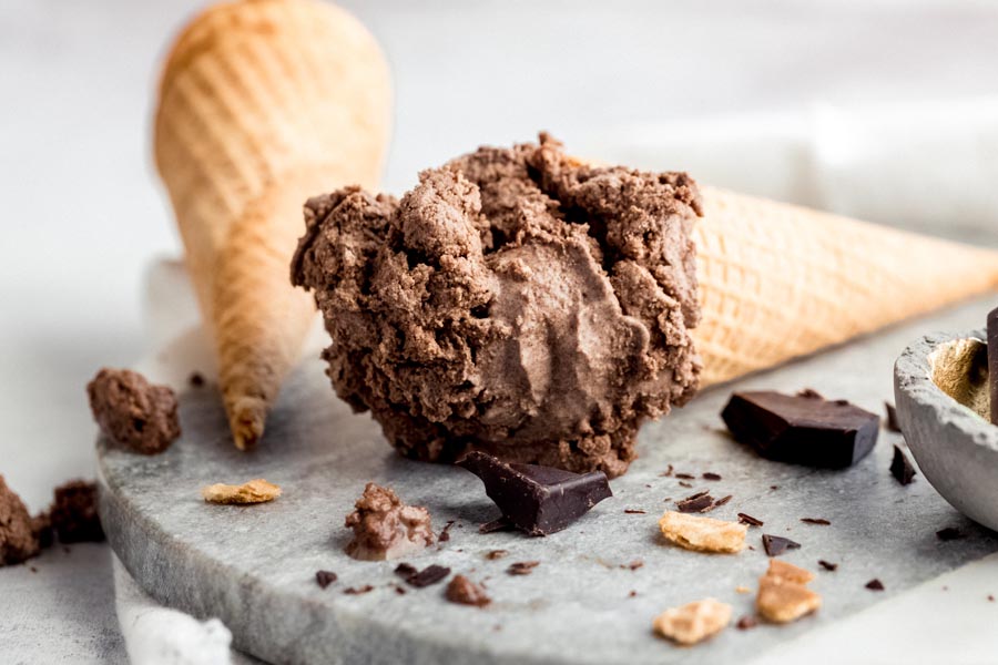 a chocolate ice cream on a marble slab with chunks of cone and chocolate in front