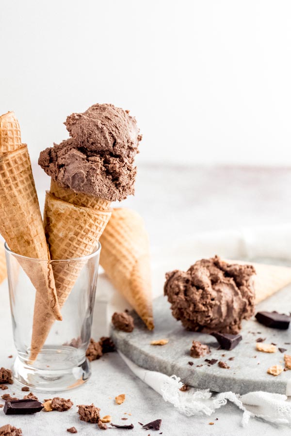 ice cream cones with chocolate ice cream on top and crumbled cone and chunks of chocolate near