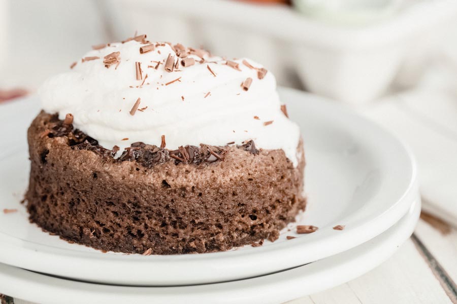 a chocolate cake on a white plate topped with whipped cream