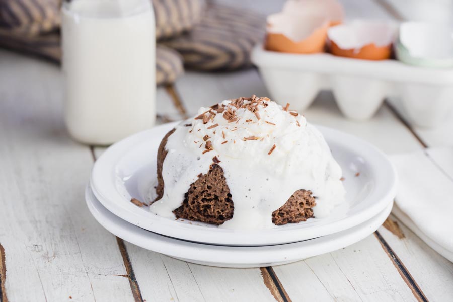 cream melting down the sides of a small cake with milk and eggs in the background