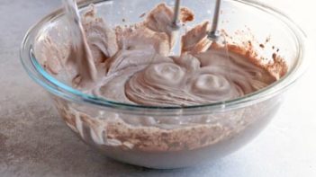 a clear bowl with chocolate whipped cream being mixed with an electric mixer