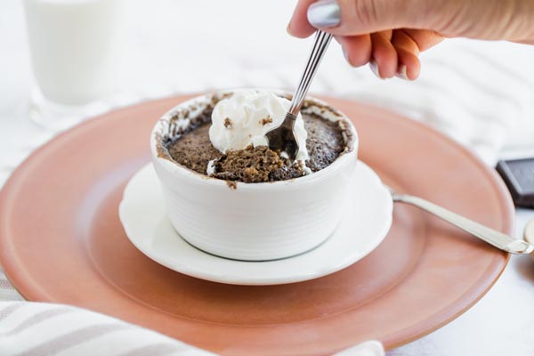 cutting out a bite of chocolate keto cake with whipped cream on top in a white ramekin