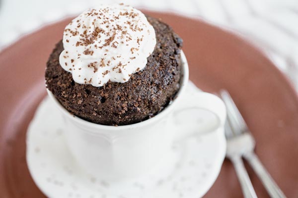 a thick mug cake popping out of a mug with a dollup of whipped cream on top