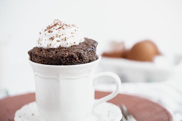 fluffy chocolate cake coming out of a white mug topped with whipped cream