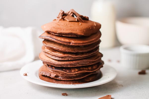 huge stack of chocolate pancakes on a white plate with a white napkin in the background